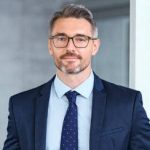 Portrait of handsome mid adult business man standing in modern office. Successful mature entrepreneur in formal clothing looking at camera with satisfaction. Confident man in suit with eyeglasses and beard standing with hands in pocket and looking at camera in office.